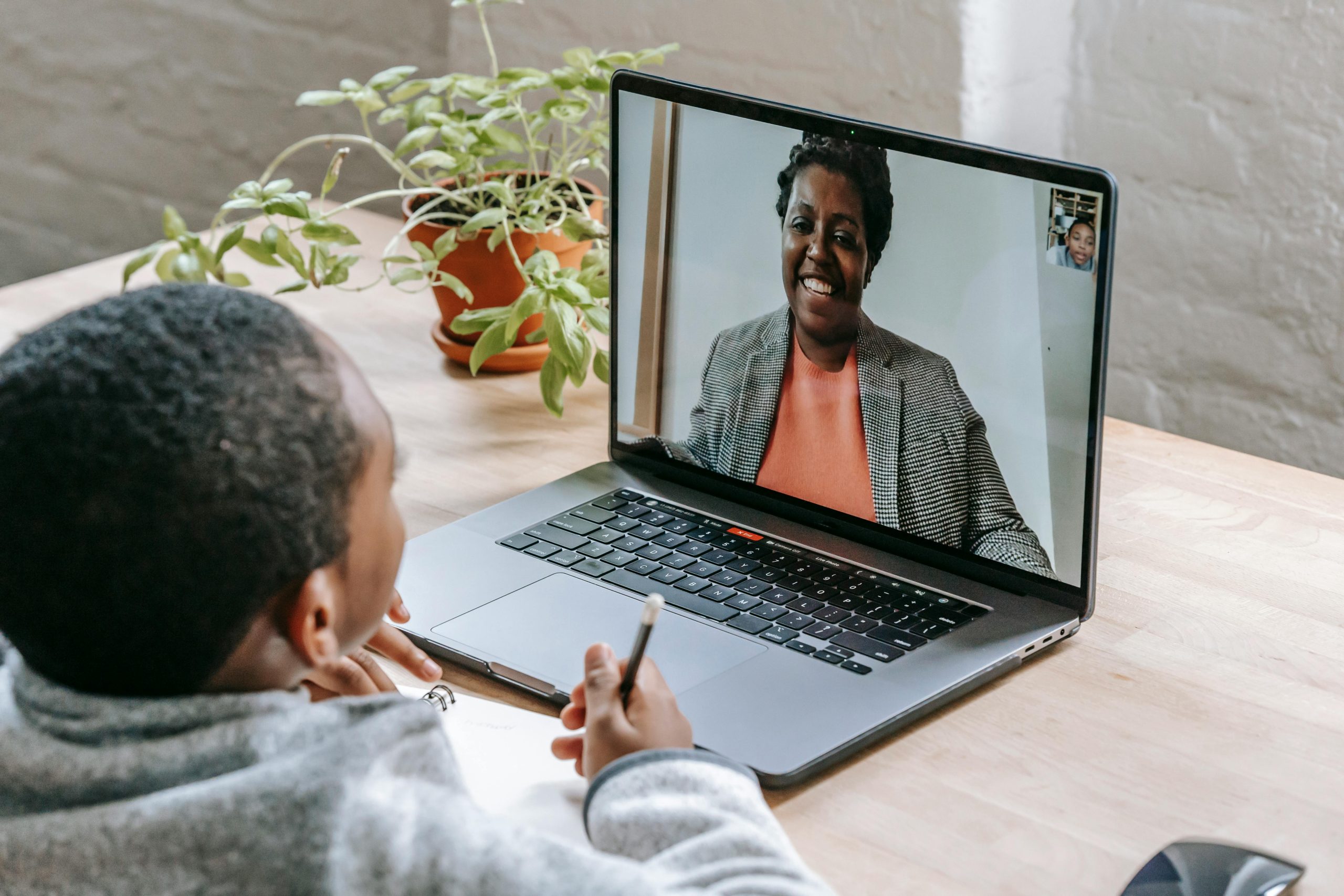 A child participates in online tutoring, focusing on a laptop screen with a smiling tutor.